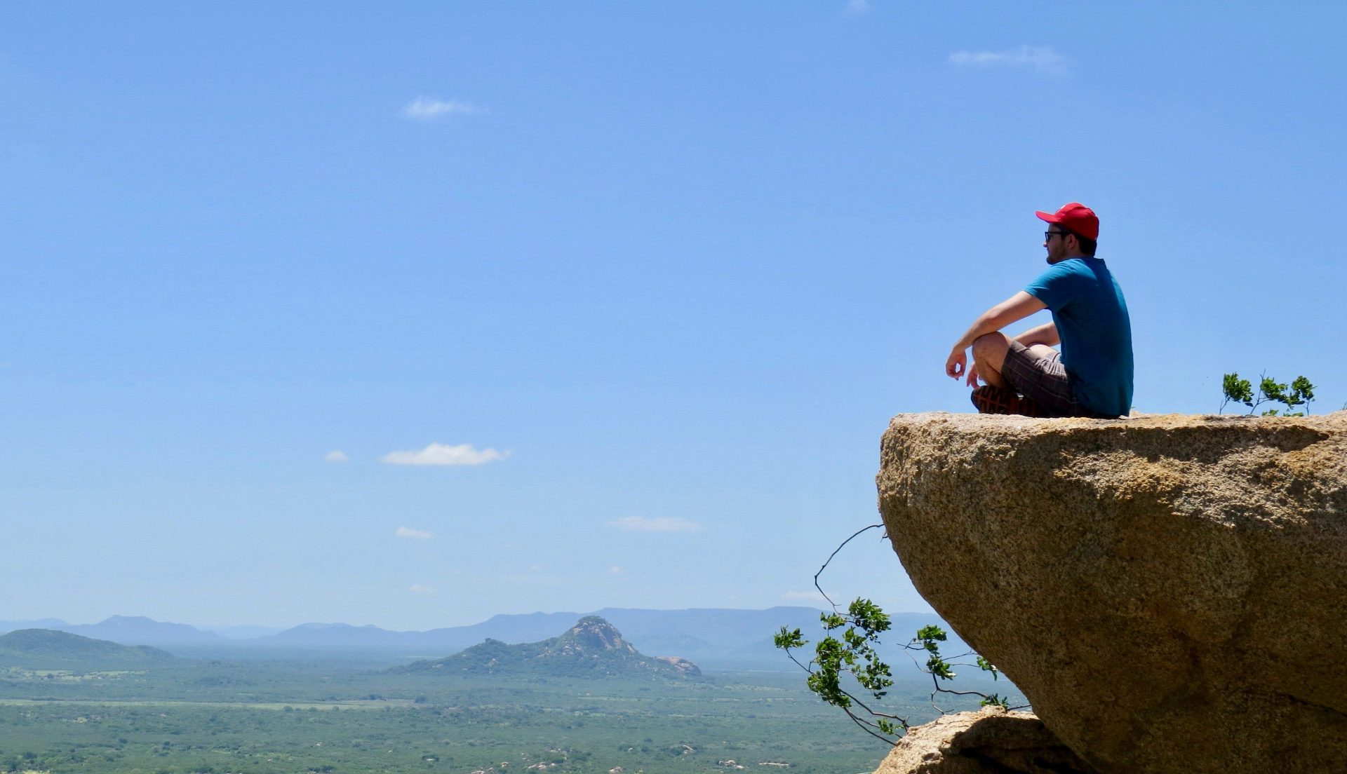 man in blue t-shirt sitting on brown rock near body of water during daytime